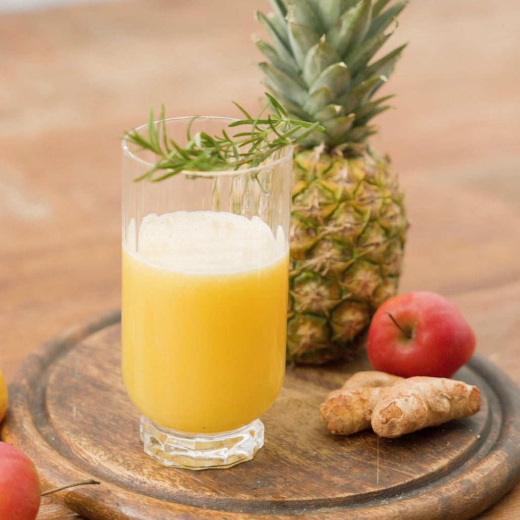 Glass of yellow juice with pineapple, apple, and ginger on a wooden board