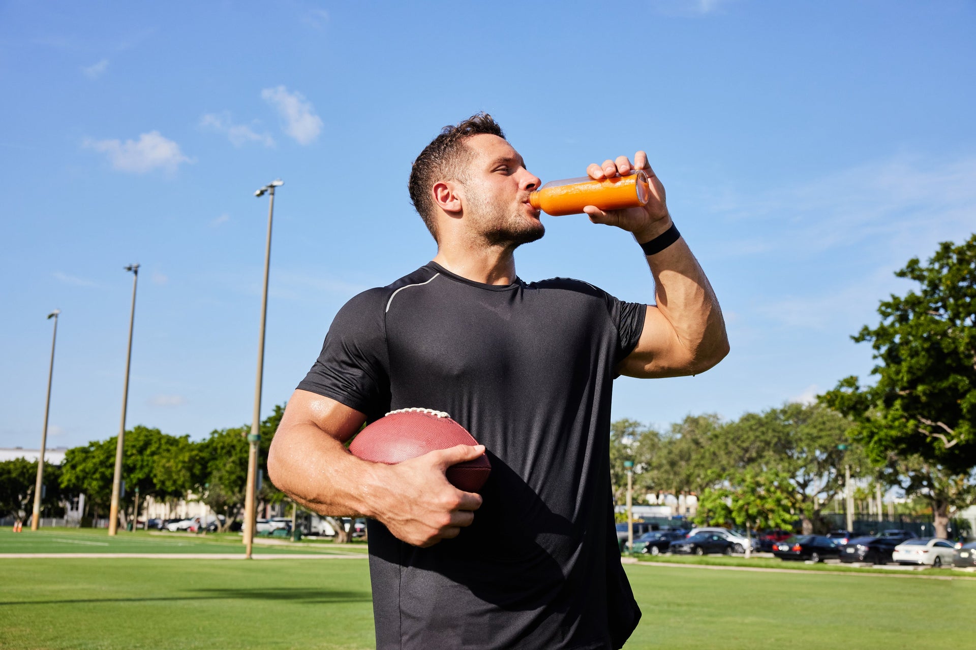 Person drinking from a bottle while holding an American football on a field