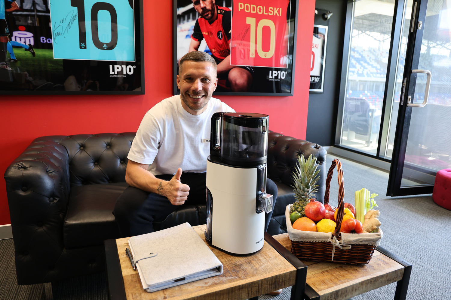 Person sitting on a sofa next to a juicer on a table with fruits and vegetables