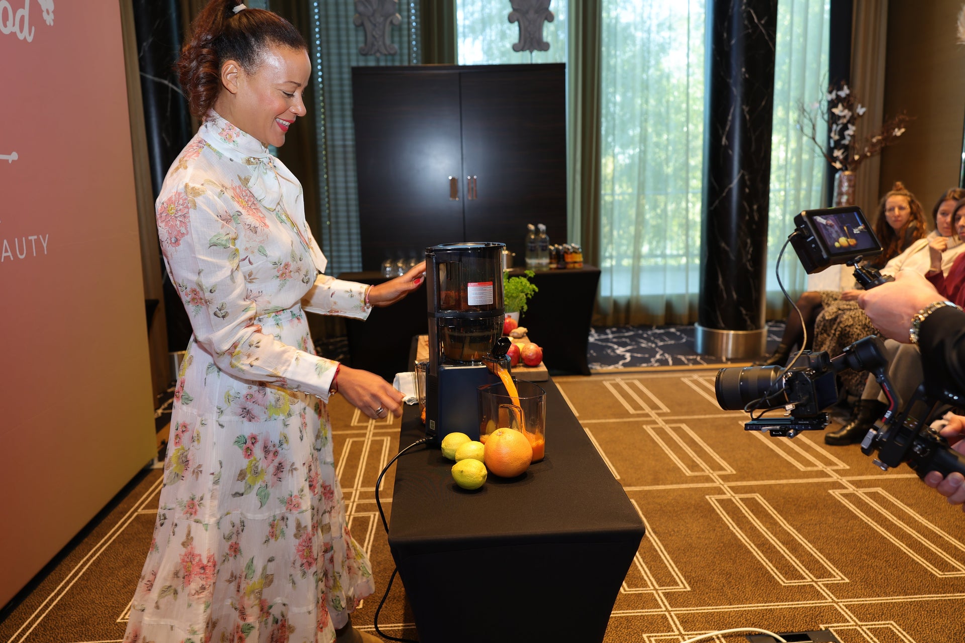 Person demonstrating a juicer on a table with fruits while others watch