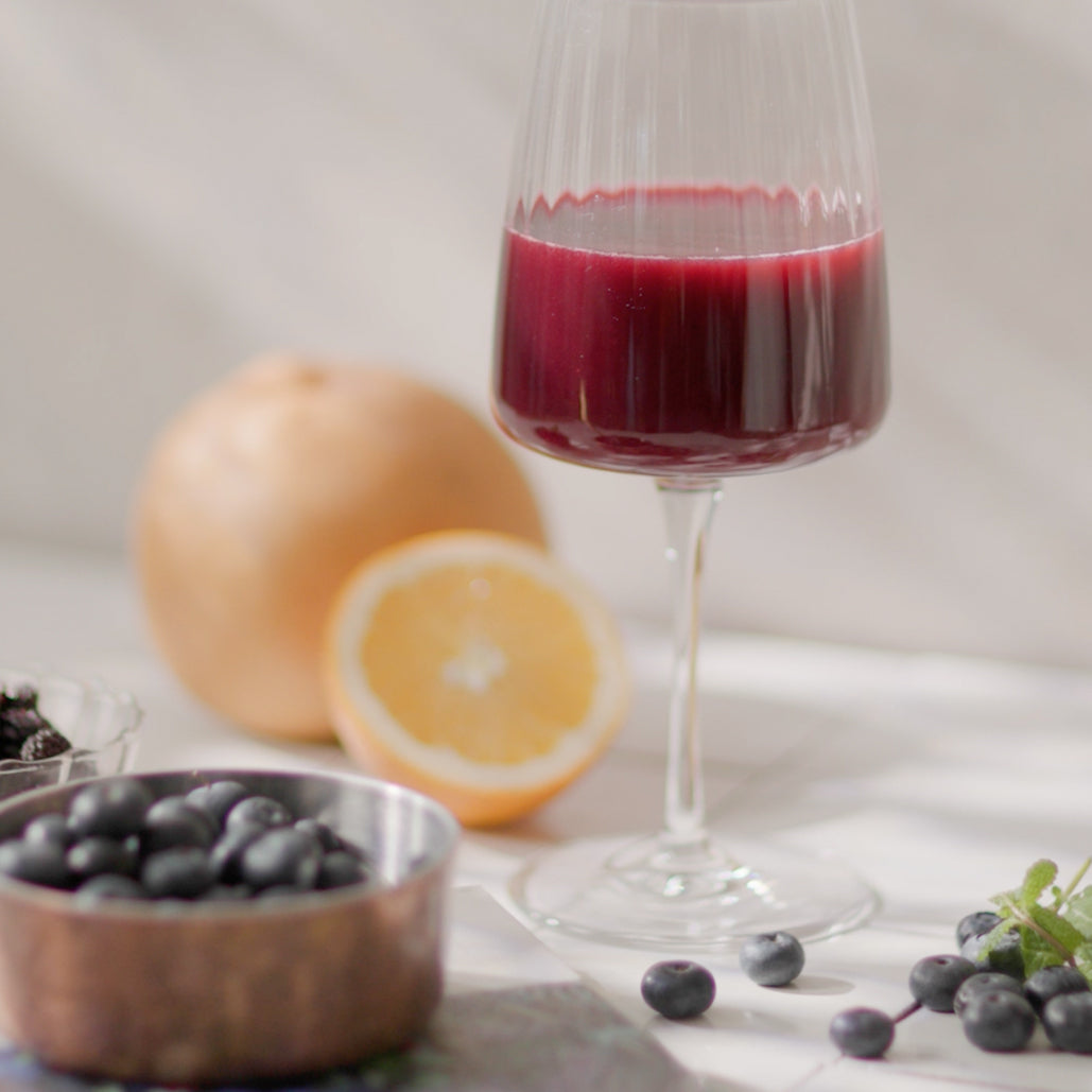Glass of dark red juice with a halved orange, pear and blueberries on a table