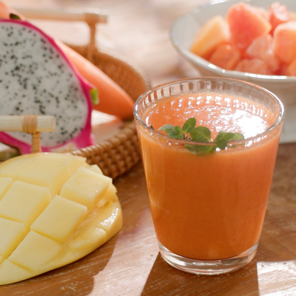 Glass of orange juice with mango, dragon fruit, and grapefruit on a table