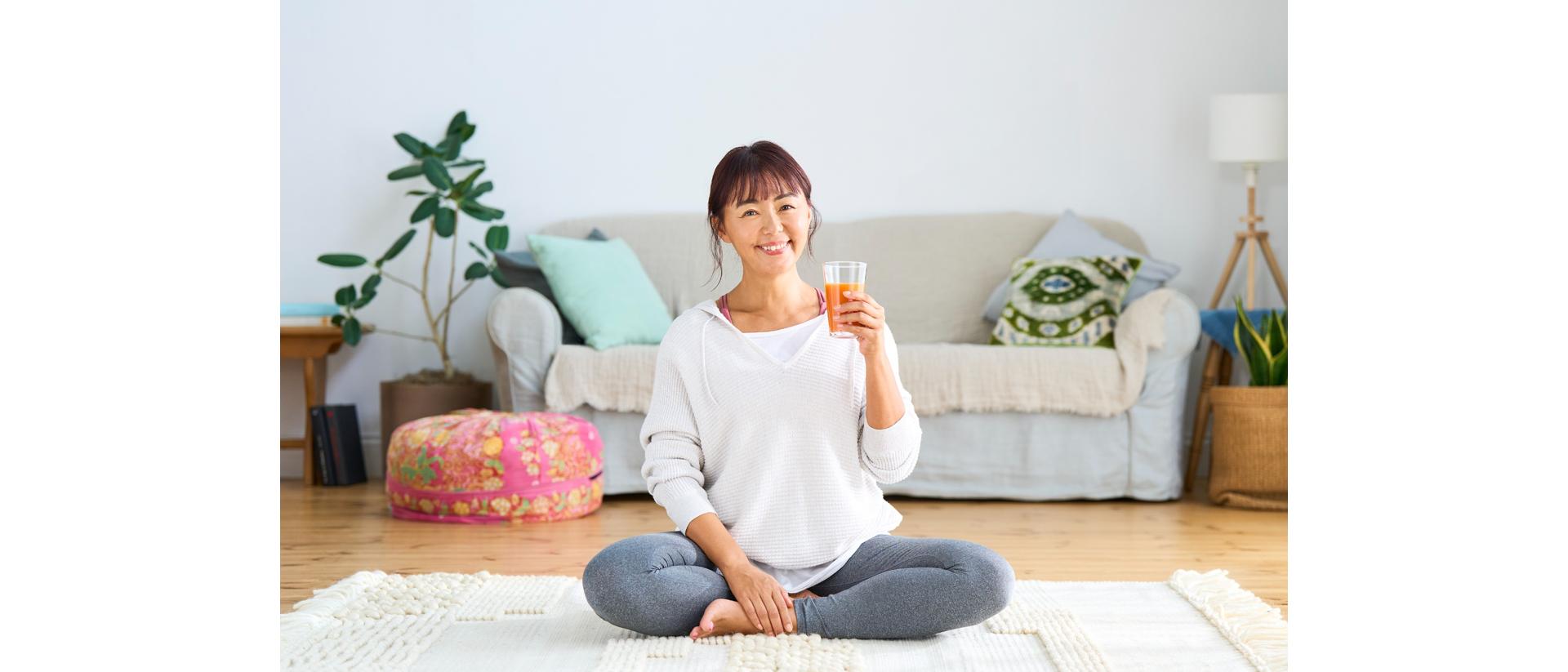 Person sitting cross-legged on the floor in a living room, holding a glass of juice