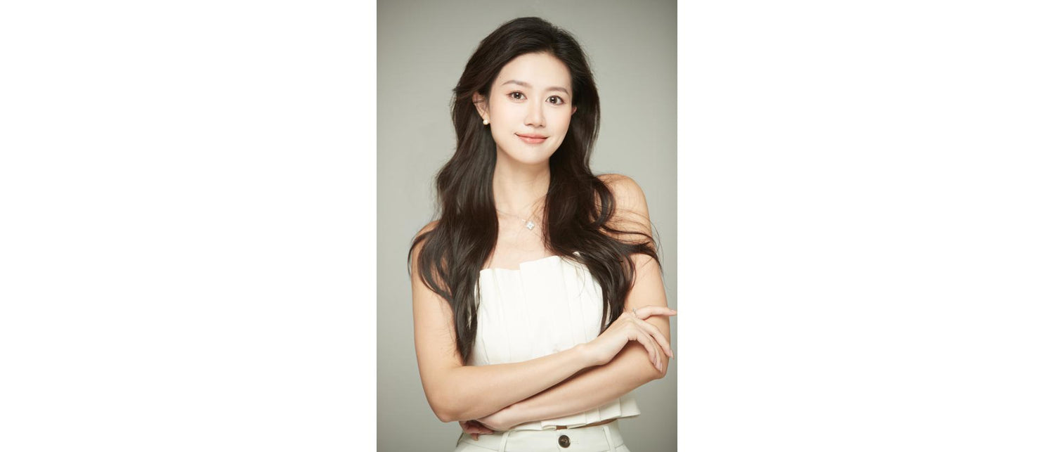 Person with long hair standing with arms crossed against a plain background