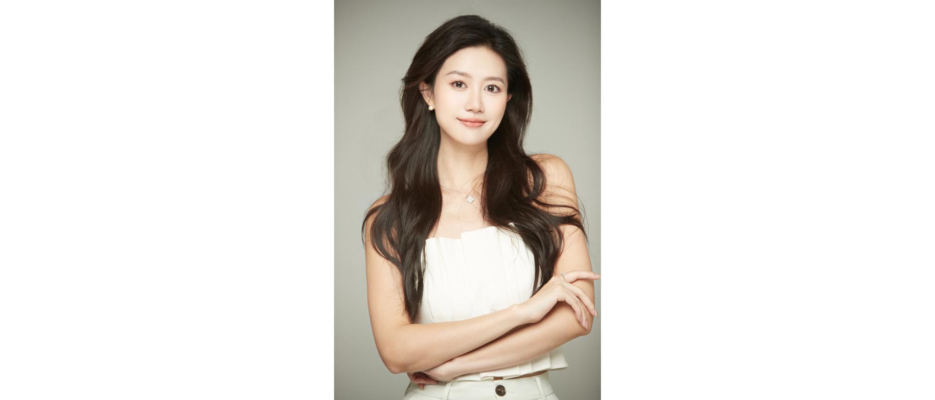Person with long hair standing with arms crossed against a plain background