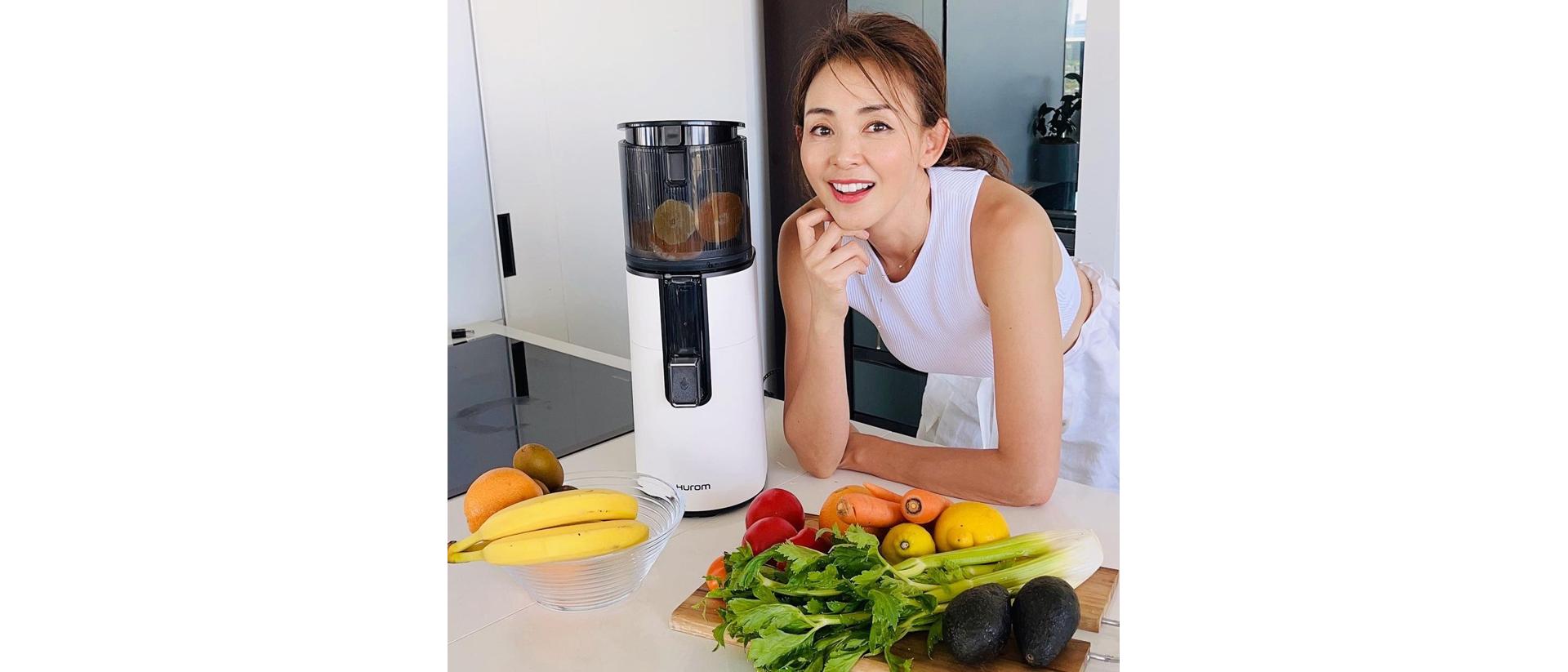 Person leaning on a counter next to a juicer with fruits and vegetables