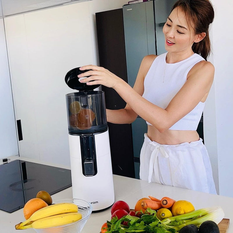 Woman using a juicer with fruits and vegetables on a kitchen counter