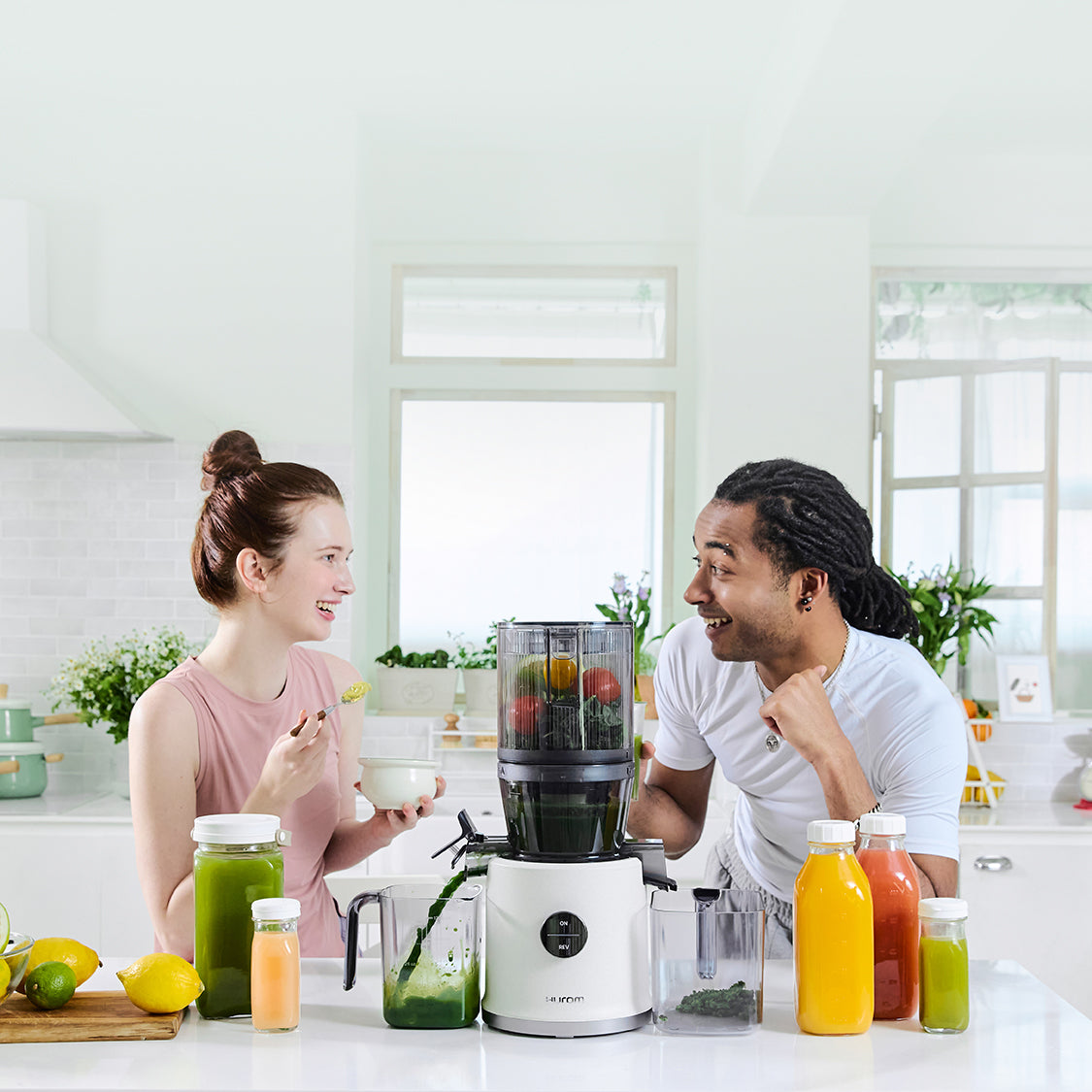 Two people in a kitchen with a juicer and various fruits and vegetables.