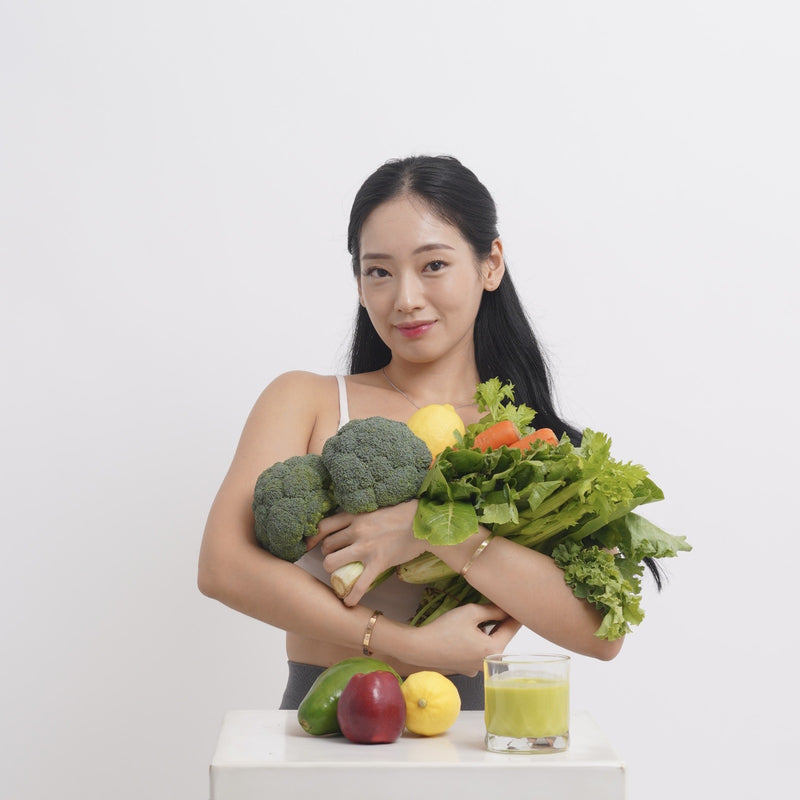 Woman holding a variety of vegetables with a glass of juice on a white background