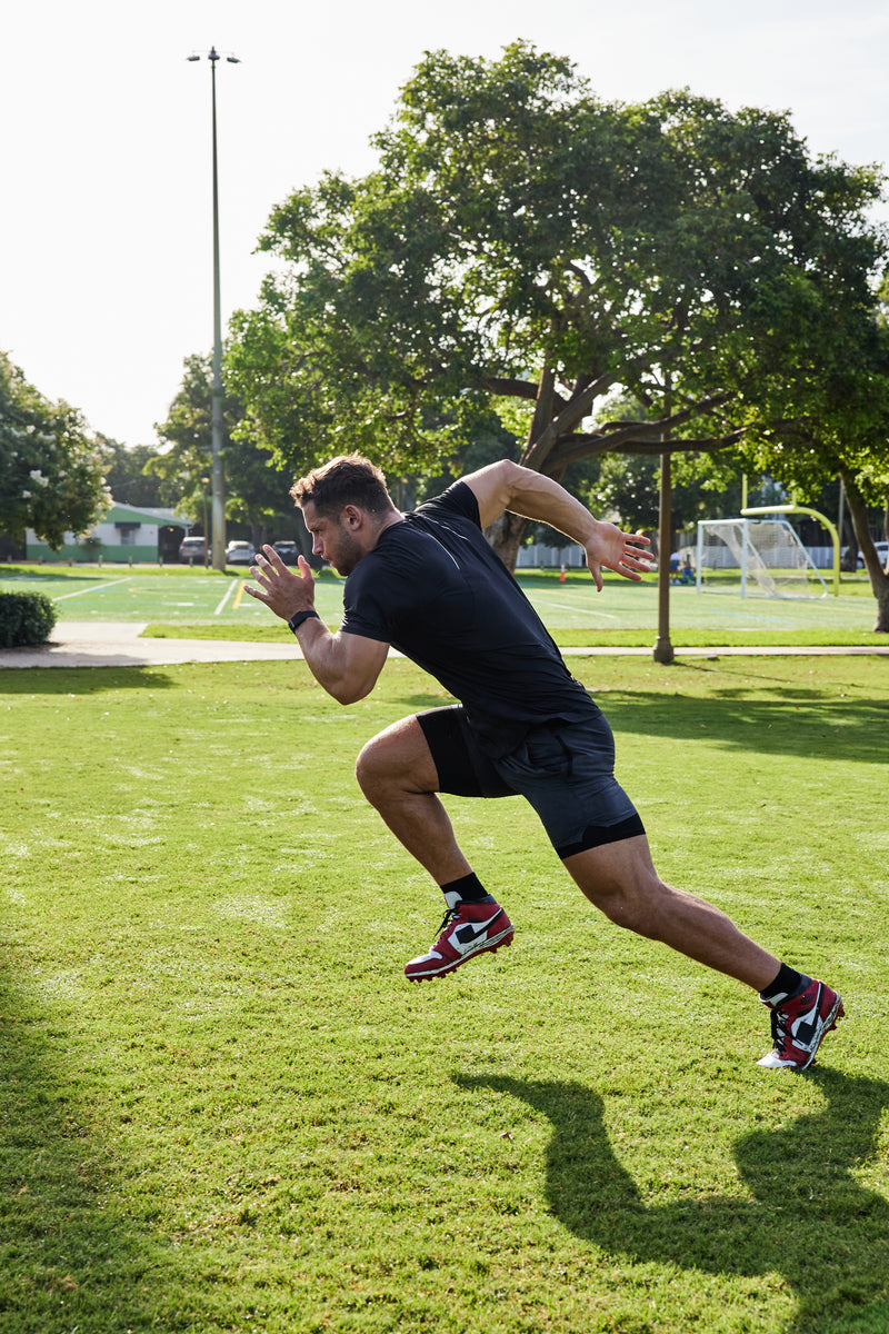 Man in athletic wear running on a grassy field with trees in the background