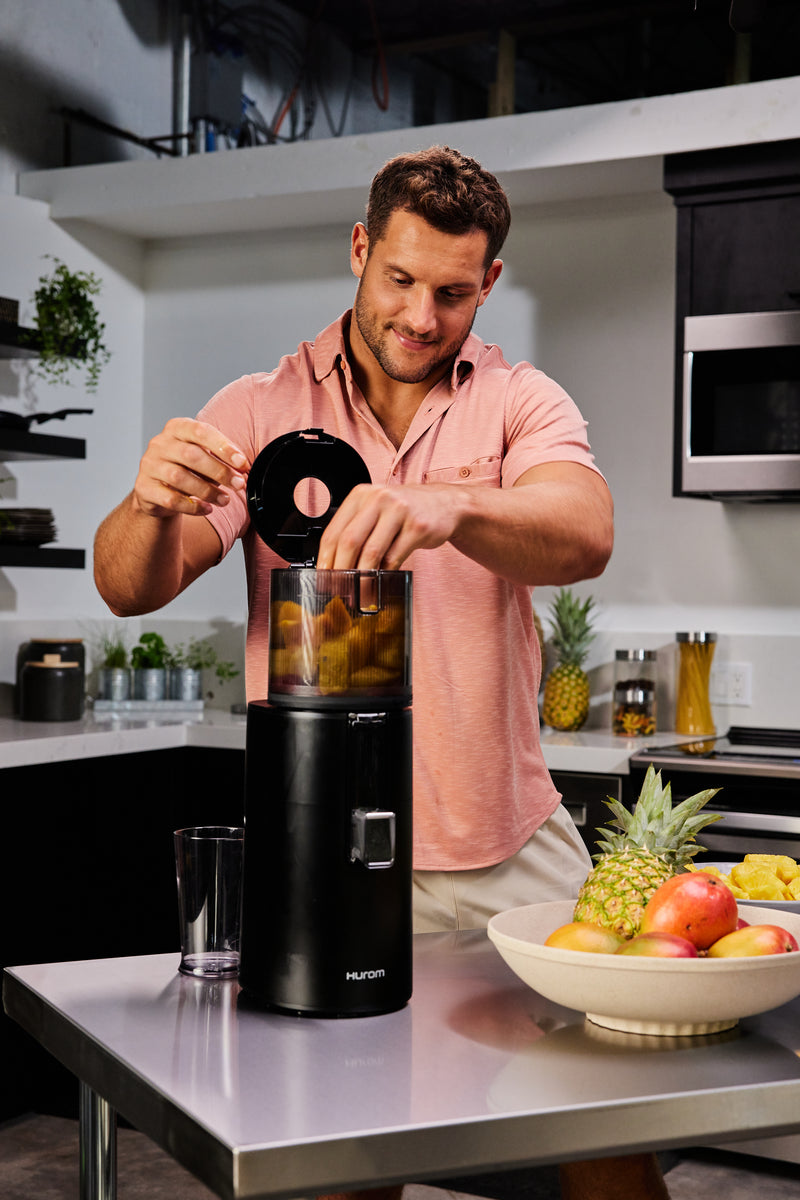Man preparing a cold pressed juice in a kitchen with a juicer and fruits.