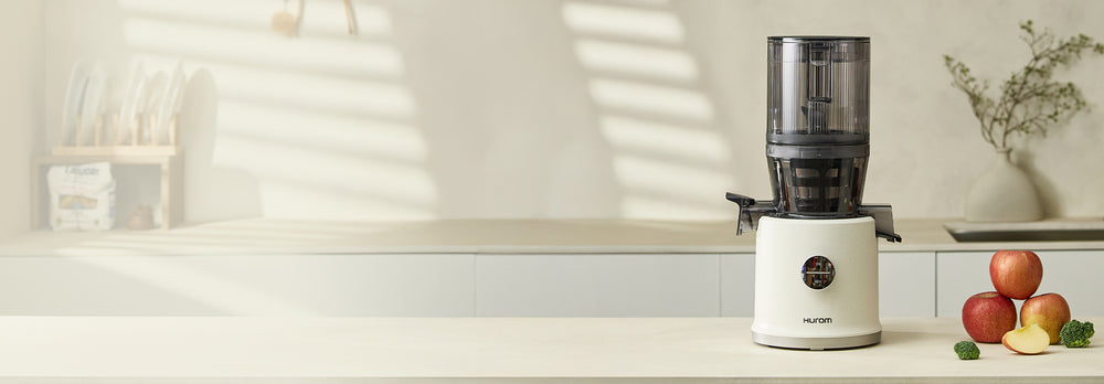White juicer on a kitchen counter with apples and a vase in the background H80ST