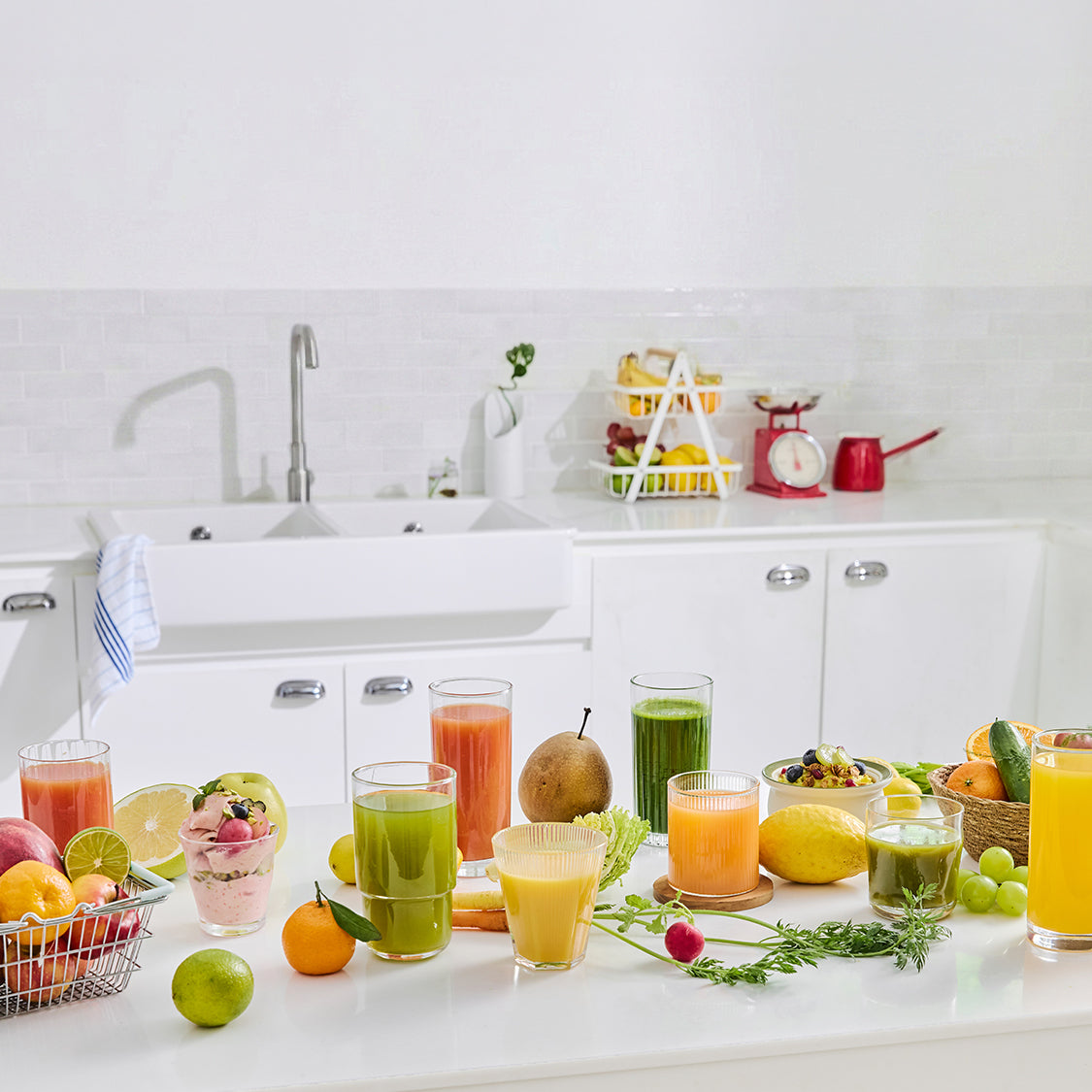 Kitchen counter with various glasses of juice and fruits on a white countertop.