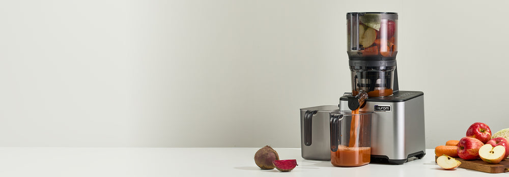 Juicer with fruits and vegetables on a white surface against a light gray background CP50