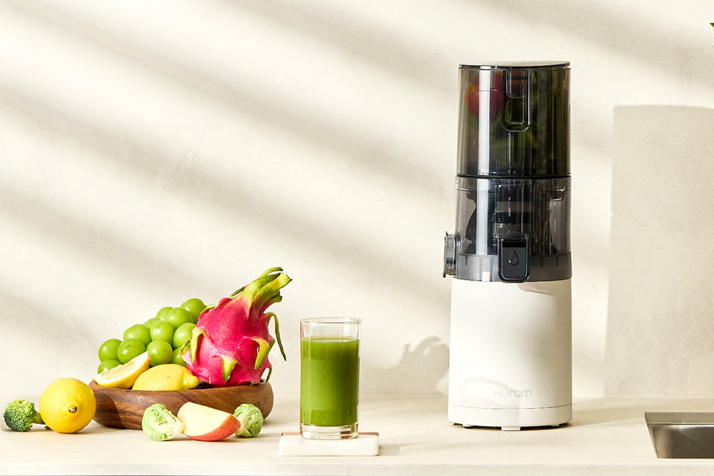 Juicer with a glass of green juice and fruits on a kitchen counter E30ST