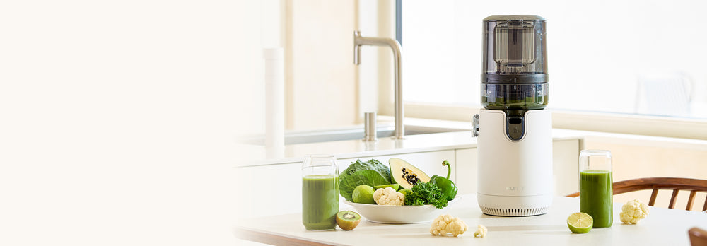 Juicer with green juice and ingredients on a kitchen counter E50ST