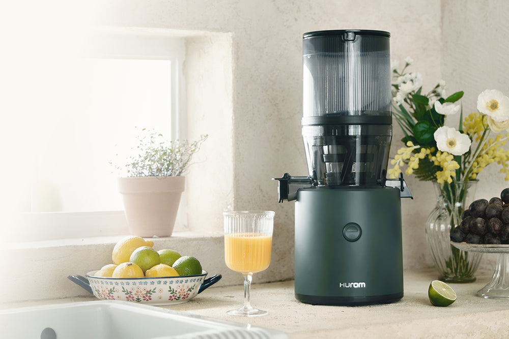 Juicer on a kitchen counter with fruits and a glass of juice. H320N