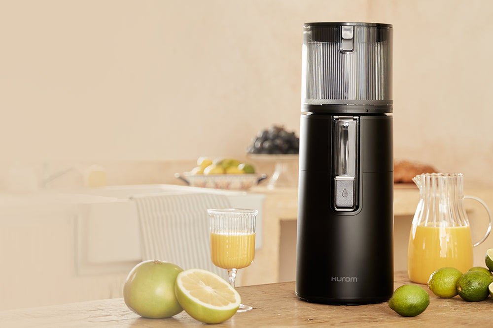 Black juicer on a kitchen counter with fruits and juice. H400