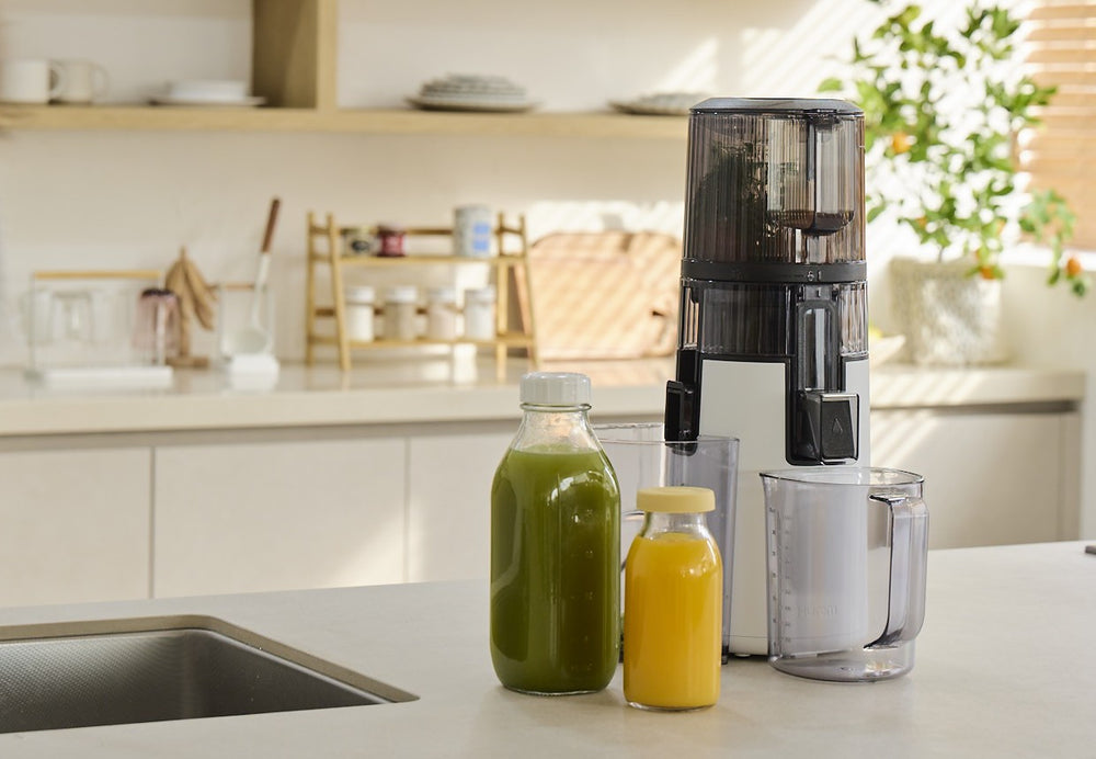 Juicer on a kitchen counter with bottles of juice and a glass. H70FT