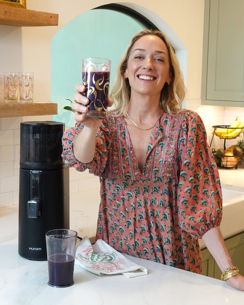 Woman holding a glass of purple juice in a kitchen setting