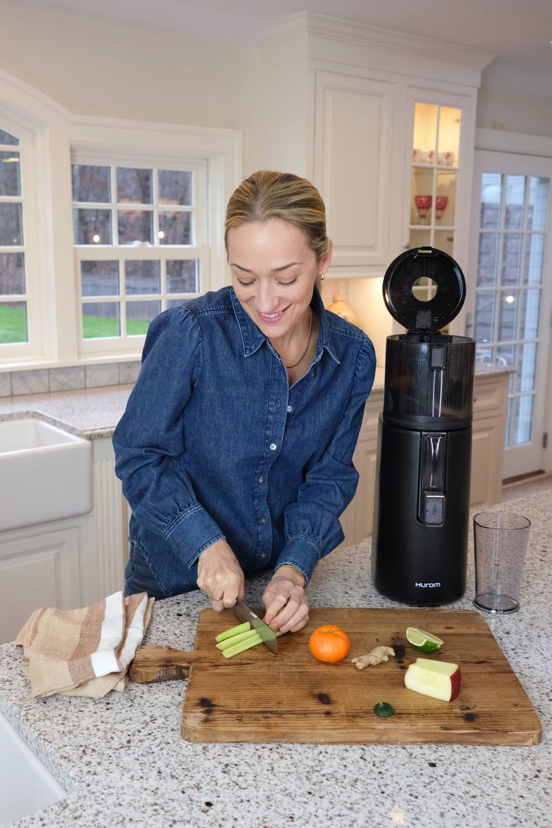 Woman preparing food on a cutting board in a kitchen with a juicer next to her.