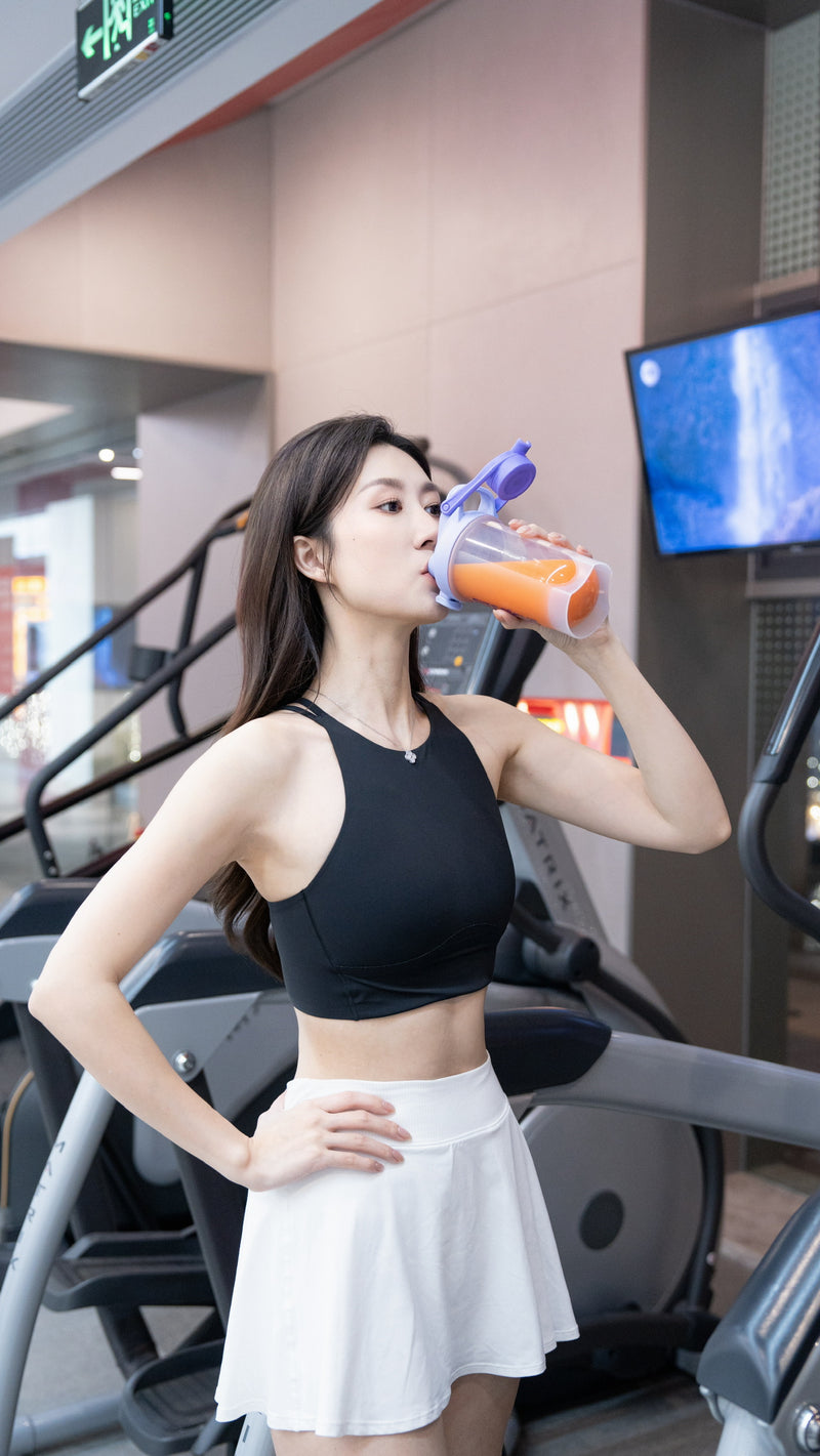 Woman in athletic wear drinking from a sports bottle in a gym setting