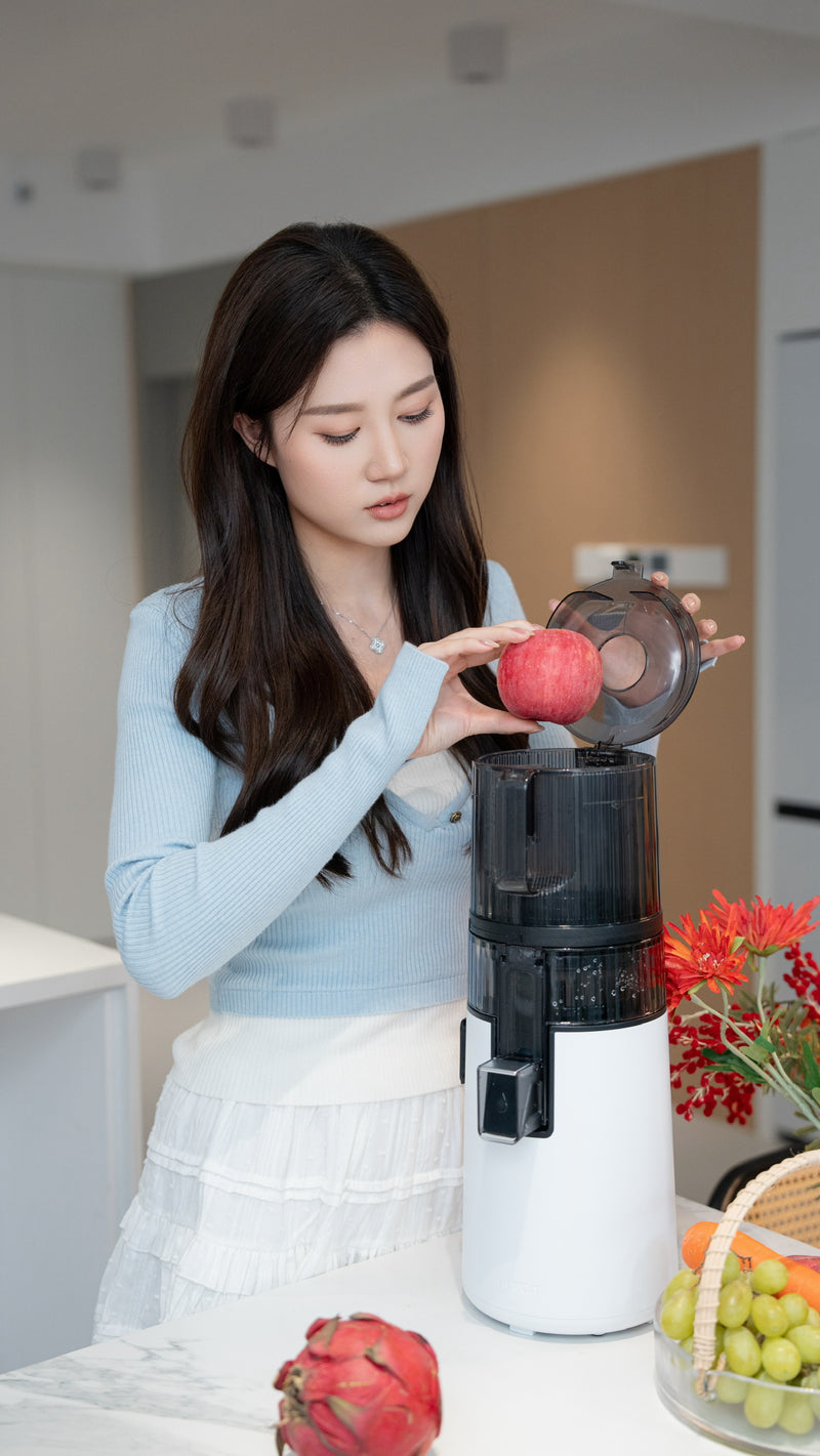 Woman using a juicer with fruits on a kitchen counter