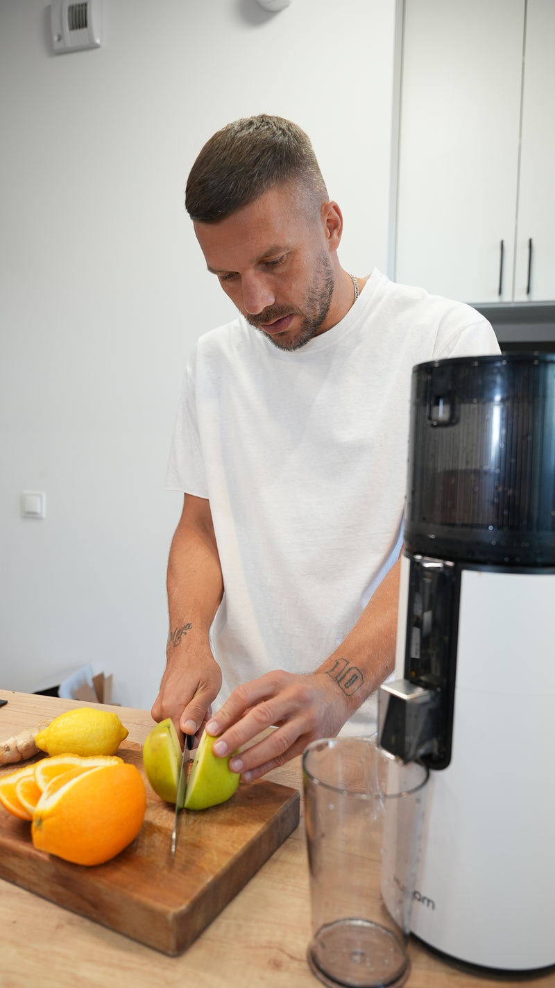 Man preparing fruit in a kitchen with a juicer and cutting board.