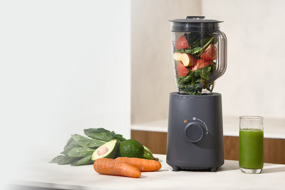 Blender with ingredients and a glass of green juice on a kitchen counter BL-E01