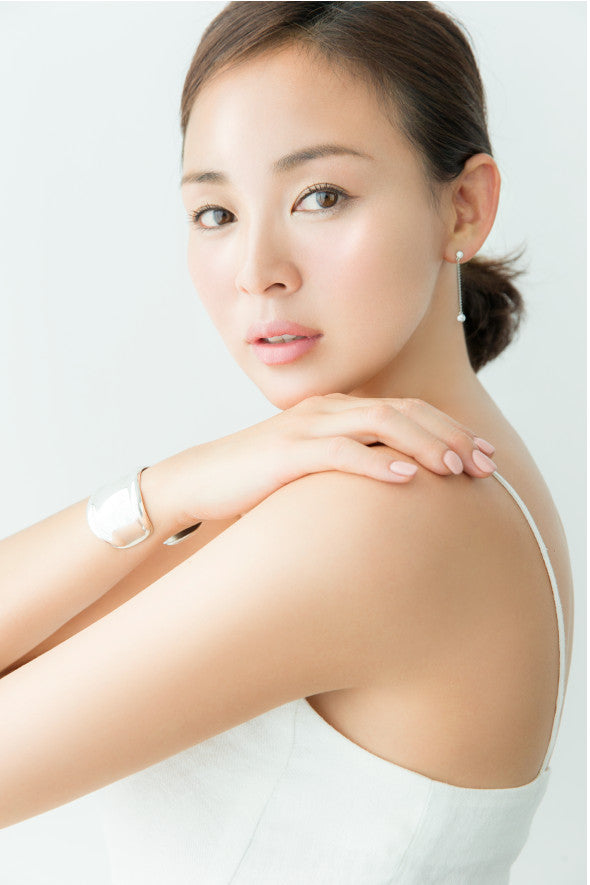 Woman with a white background, wearing a white sleeveless top.