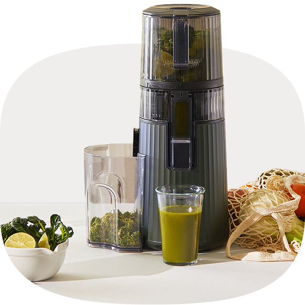 A charcoal gray Hurom juicer on a minimalist white counter, representing the brand's story of preserving nature's original nutrients. A glass of vibrant green juice and fresh ingredients like lemons and kale illustrate the "Farm to Glass" philosophy.